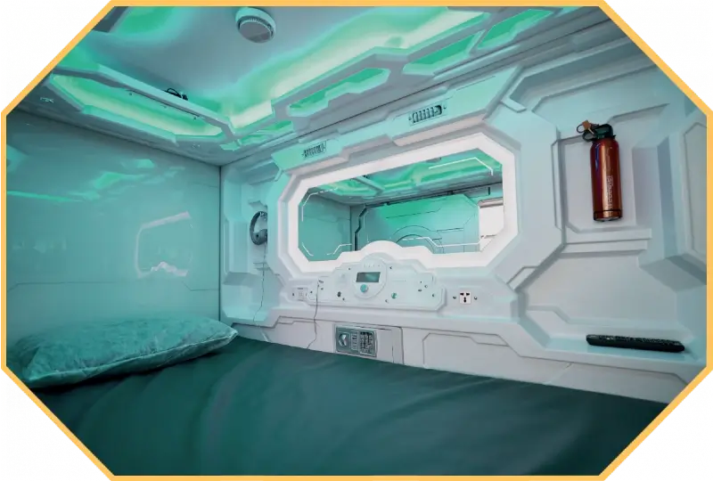 the interior of a futuristically styled hotel capsule with a single bed. Teal lighting shines from the ceiling.